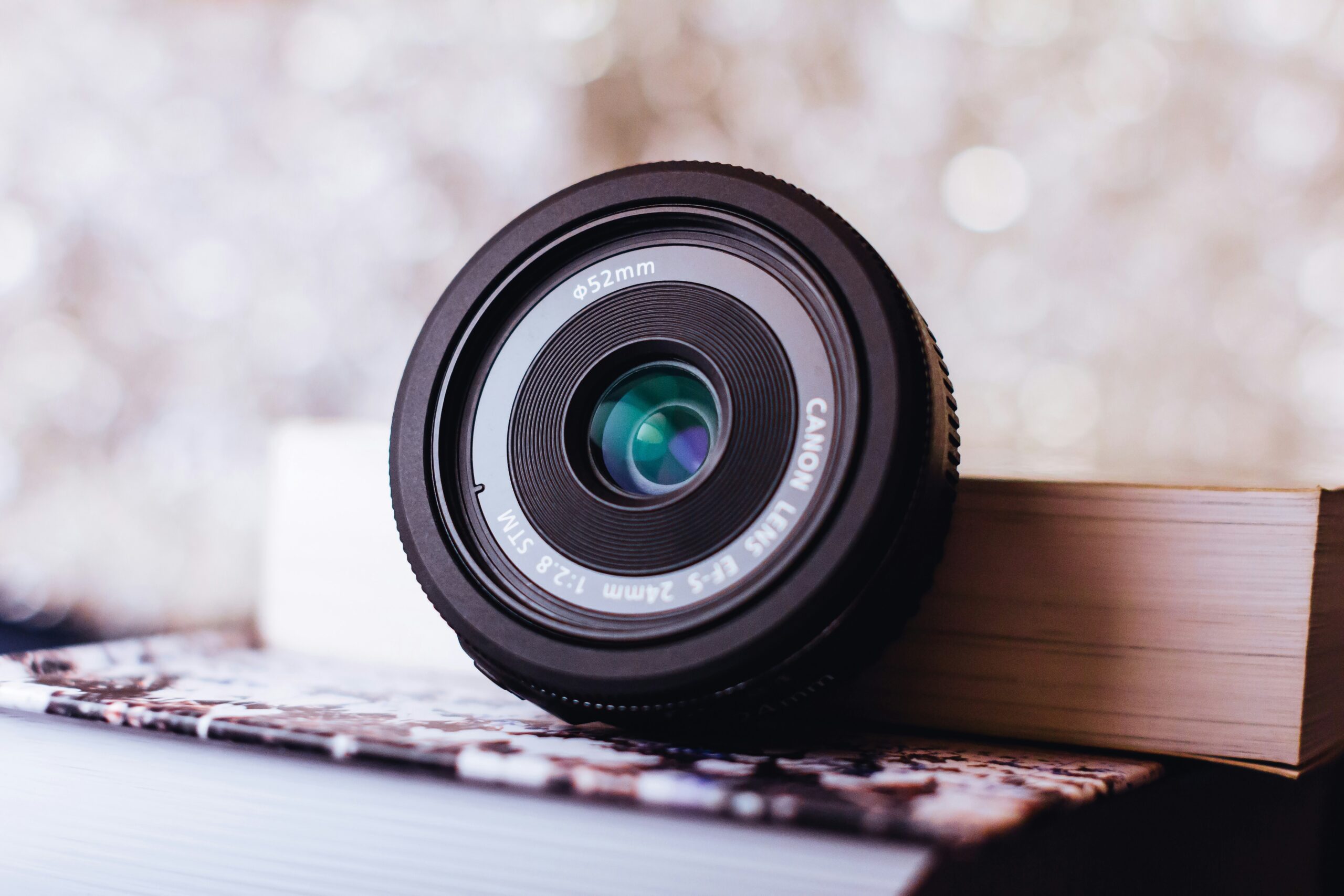 black Canon camera lens leaning on white book